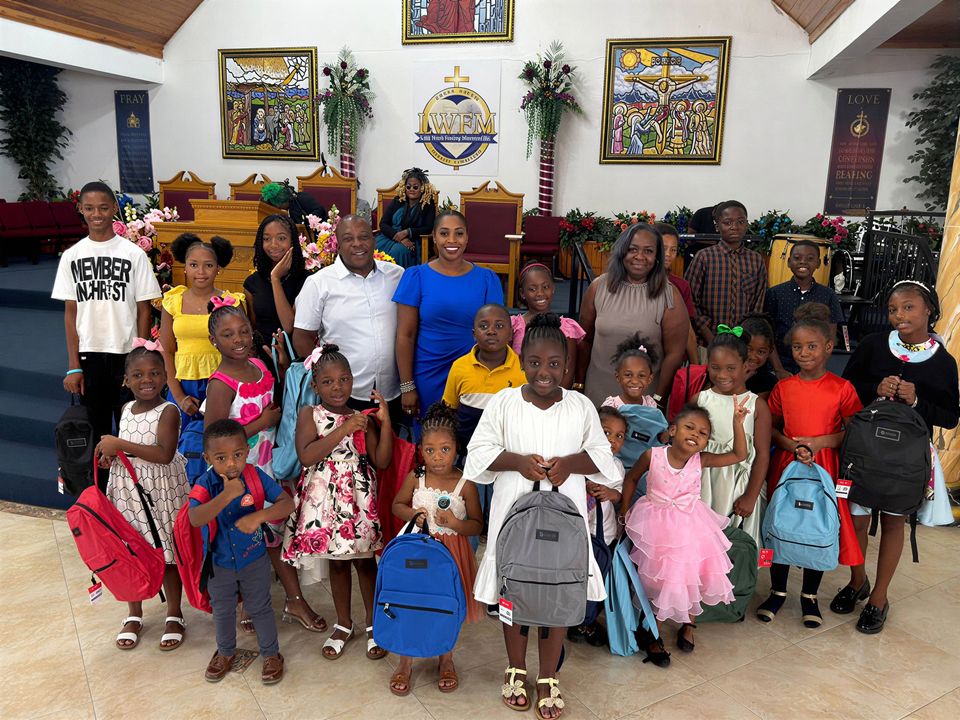 Children in church clothes holding new backpacks pose with adult leaders in front of the church altar